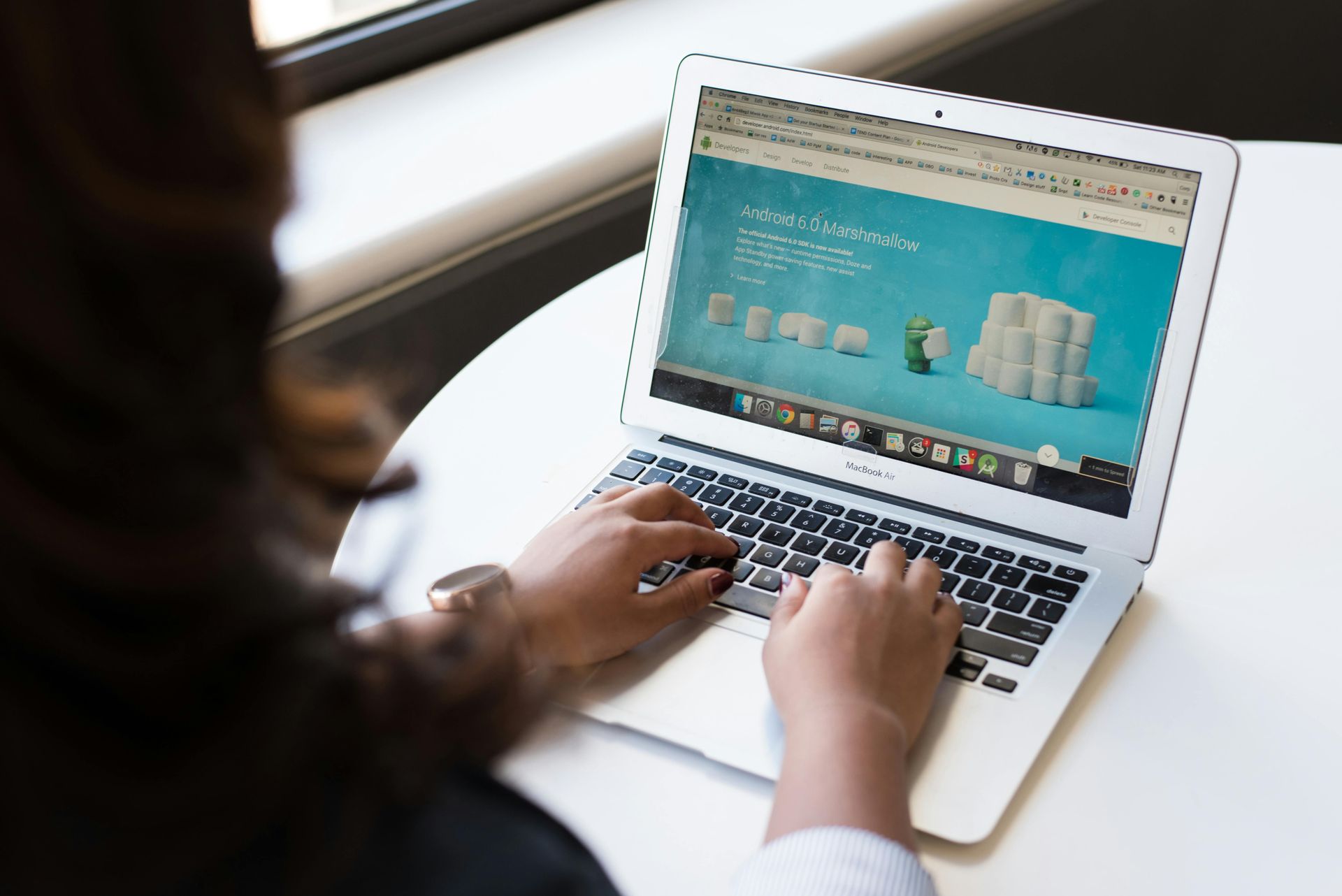 Person typing on a laptop displaying a turquoise webpage beside a window.