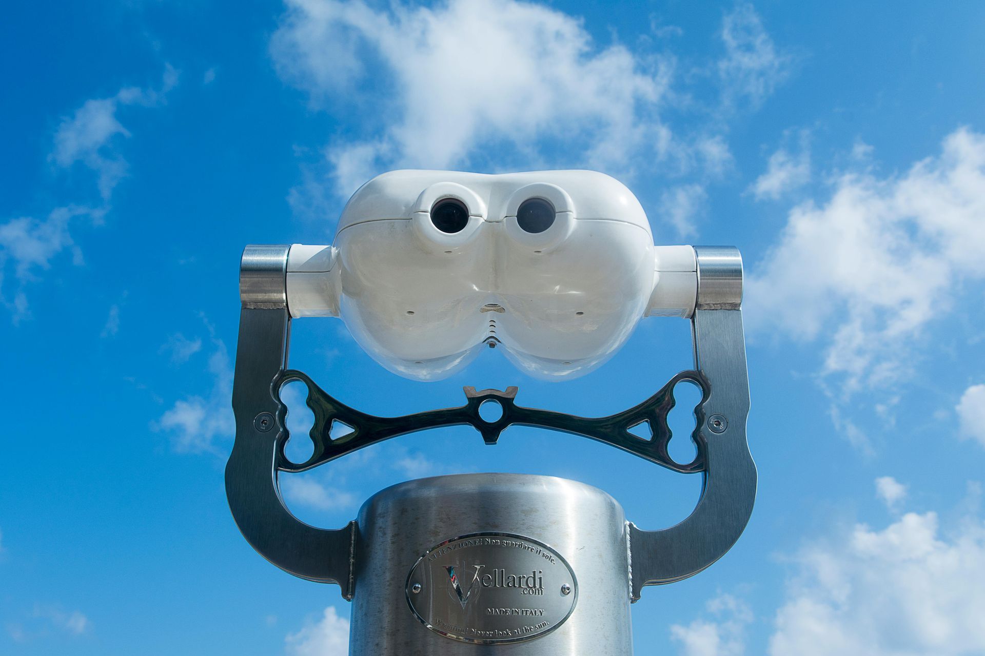Silver coin-operated binoculars against a blue sky with clouds