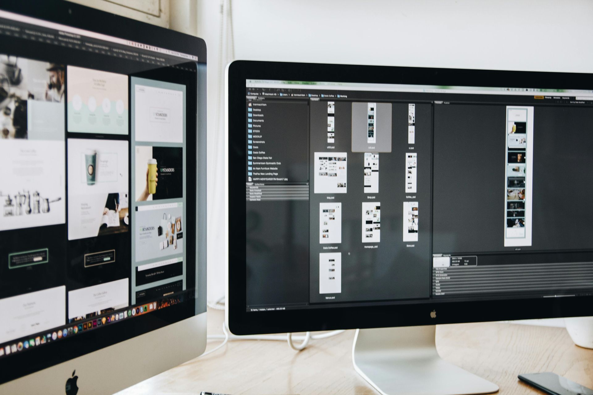 Two desktop monitors showing design software with multiple layouts on a desk.